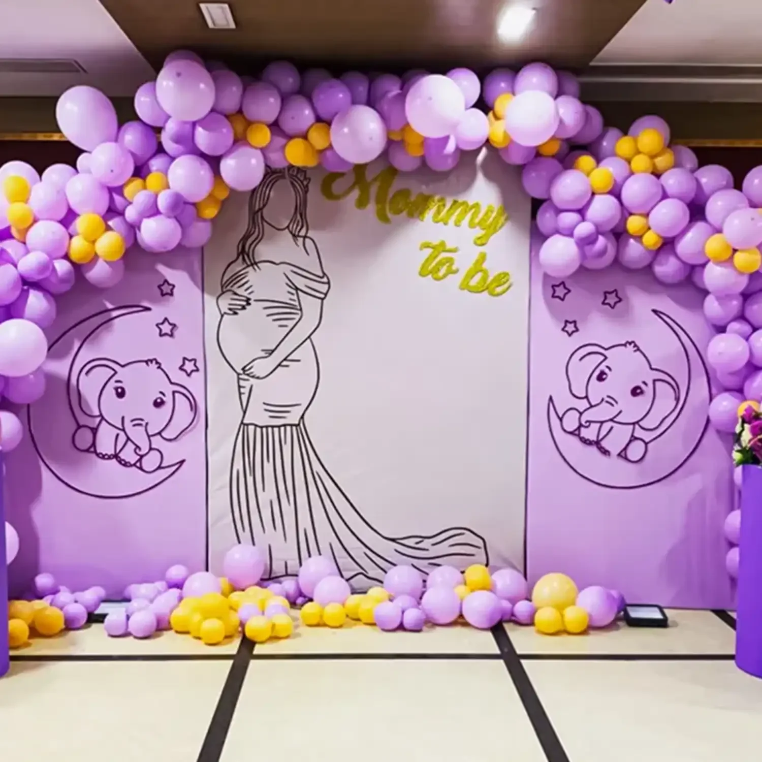 Lavender and gold balloon arch baby shower backdrop with a hand-drawn mommy-to-be illustration
