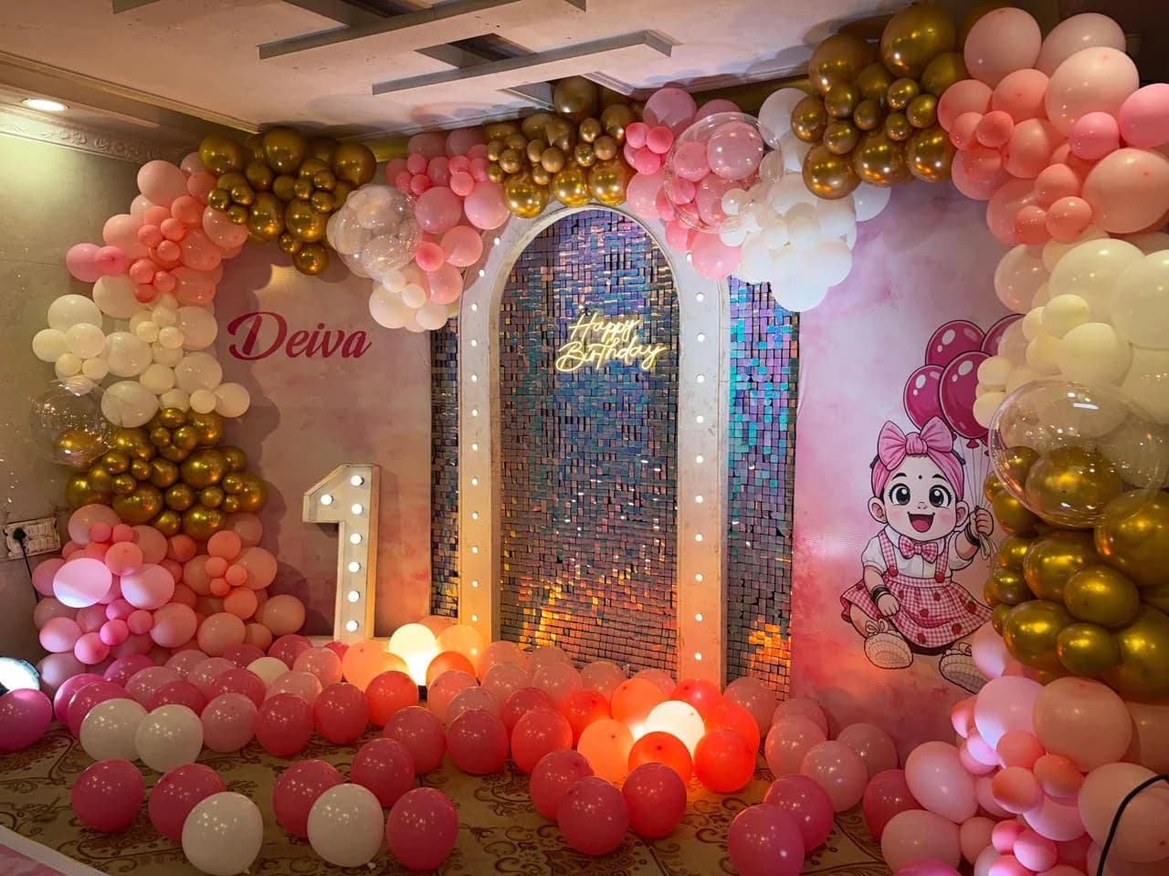 Pink and gold balloon arch birthday backdrop with a personalised name and a lit number one marquee